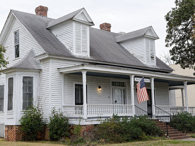 A white and gray house with an American Flag hanging in front of the front door. 