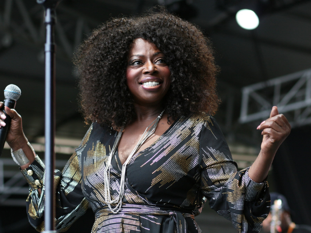 Angie Stone performing in a black, gold, silver, and pink dress. 
