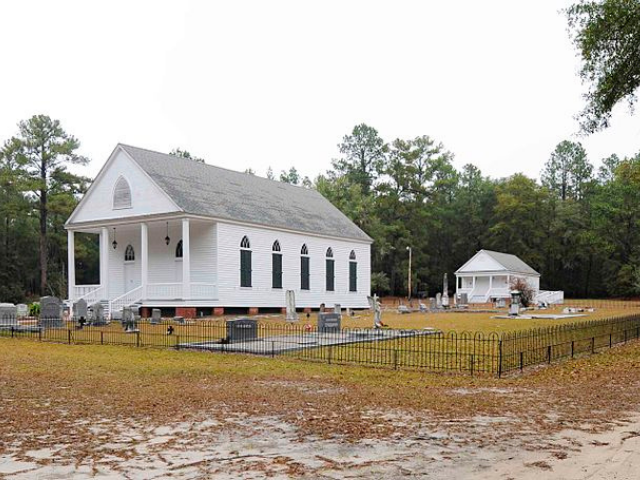  A white church surrounded by a black fence and gray grave stones. 
