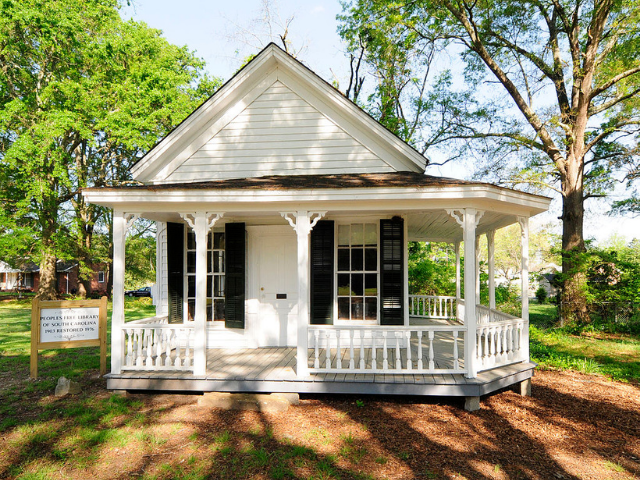 a small white house with a half wrap around porch.
