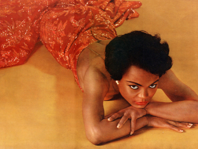 Eartha Kitt laying on an orange floor in a sparkly red dress. 