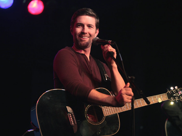 A smiling Josh Turner holding a guitar and singing into a microphone. 