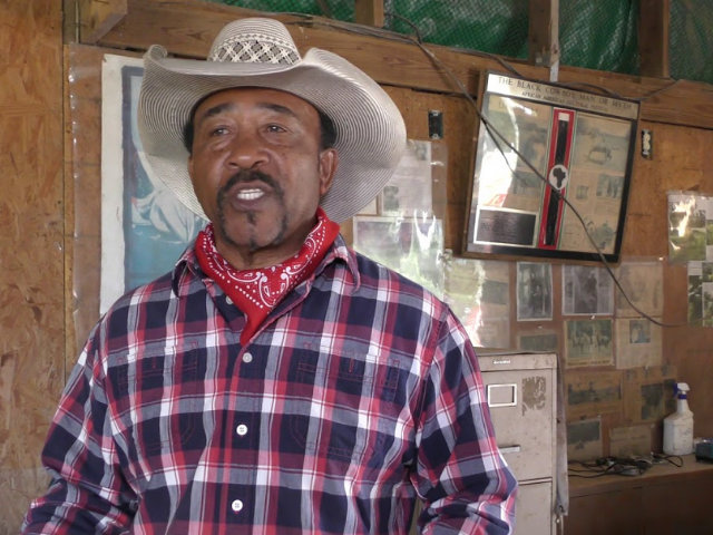 Mark Myers wearing a tan cowboy hat, red and white bandana, and a red, white, and blue plaid shirt. 
