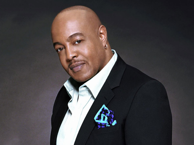 Peabo Bryson in a dark suit with a light dress shirt, and colorful dark and light blue handkerchief. 
