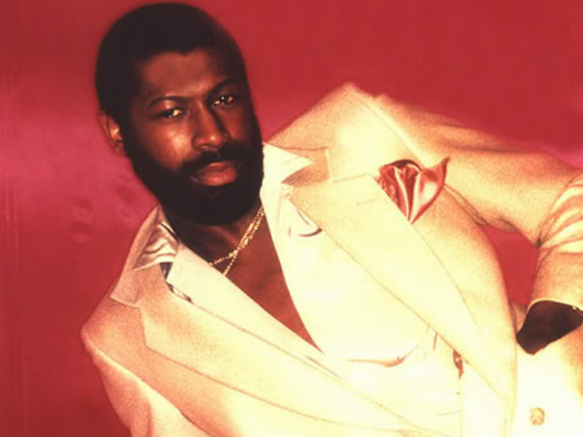 Teddy Pendergrass lounging in metallic gold suit with a silky red background. 
