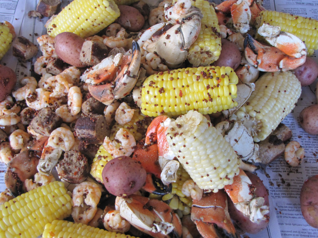 Cooked corn, potatoes, crab, and shrimp laying on newspaper. 