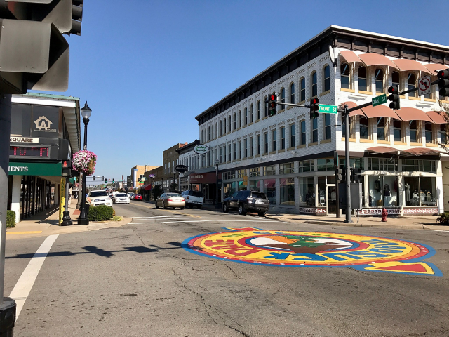 A large blue, red, orange, yellow, white, and green mural is in the center of intersection. Buildings line the street near the mural.