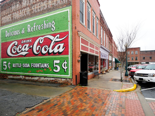 A brick building with a huge drink Coca-Cola art mural. 