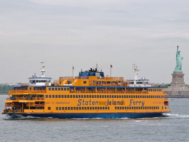 A large yellow and blue boats on the water near the Statue of Liberty 