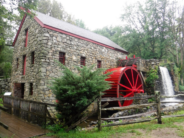 A stone building with a red mill wheel. 