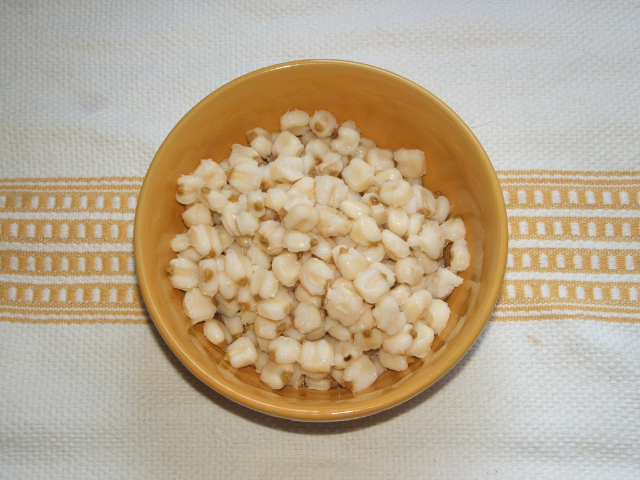 A yellow bowl with cooked off-white corn kernels on a white and gold patterned cloth. 