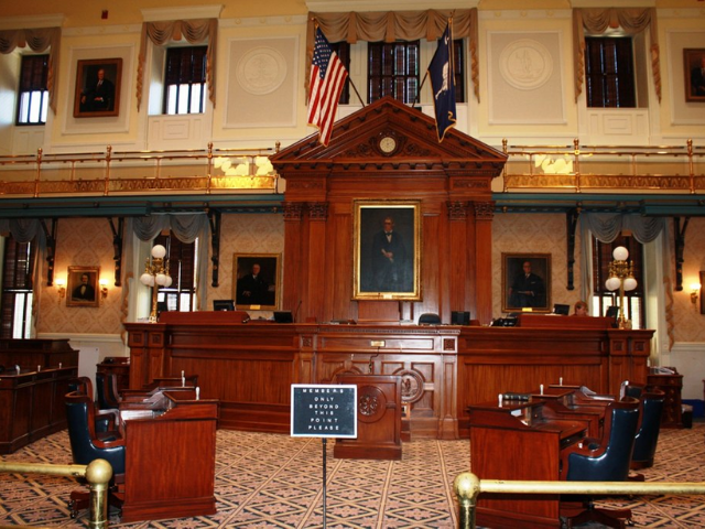 A room in various shades of browns and gold. In the center is a large wooden desk with the American and SC State flag. 