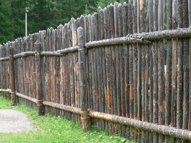 A tall fence made out of brownish-gray wooden stakes 