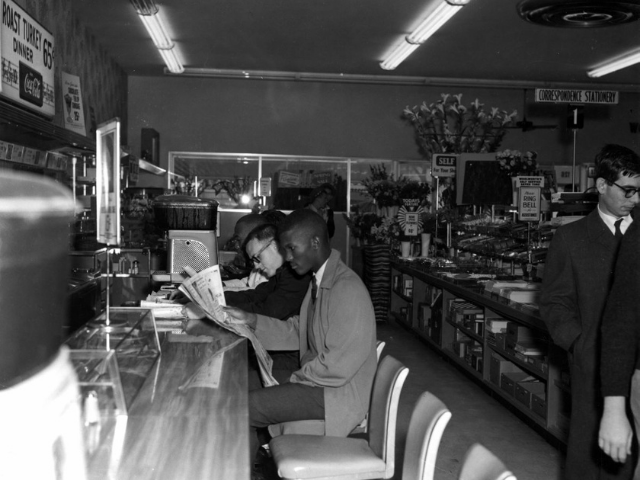 A young black man and white man sit beside each other at the lunch counter