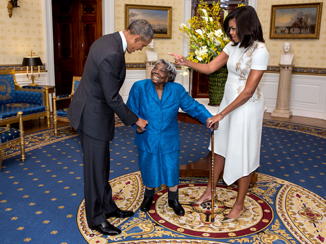 Smiling Virginia McLaurin in the middle between Barack and Michelle Obama in the Blue Room of the White House. 