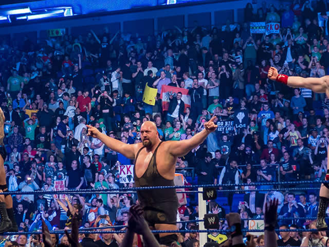 The professional wrestler The Big Show with his arms raised in the ring in a crowded arena.