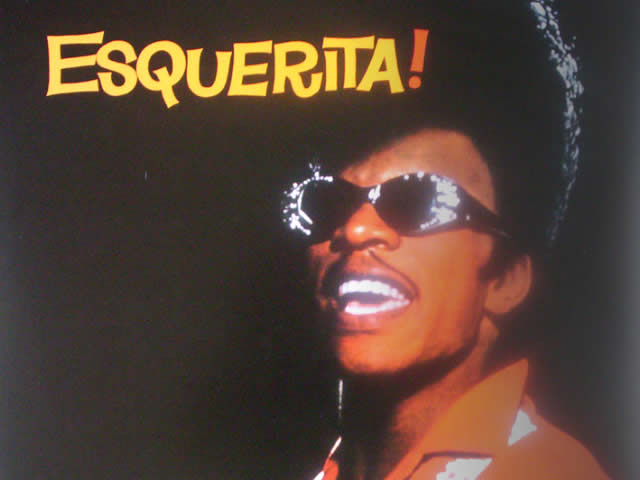 A black man with bejeweled sunglasses, a thin mustache and a pompadour.