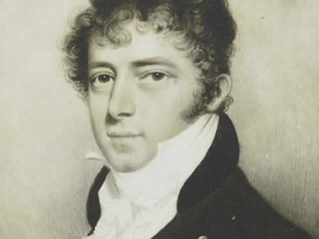 A man with curly hair wearing a black coat and white necktie.