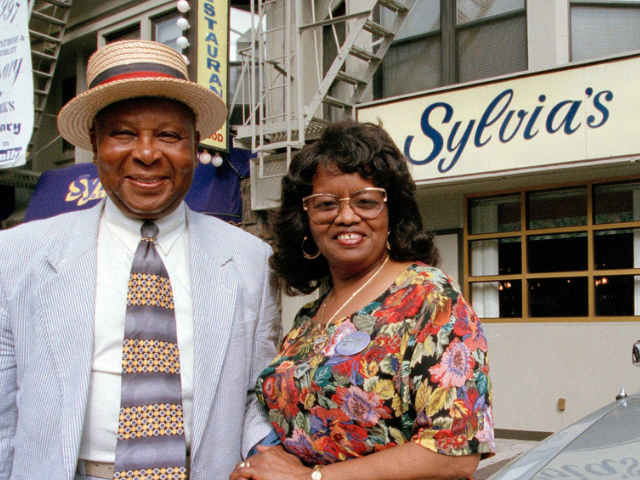 color photograph of Sylvia Woods and her husband standing in front of her restaurant