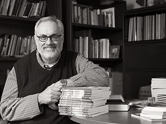 Black and white photograph of Lott sitting at his desk with shelved books in background
