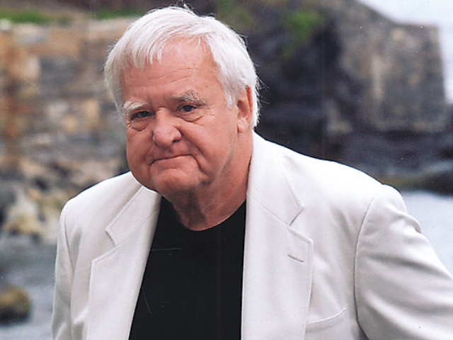 Color photograph of John Jakes wearing a black shirt and white jacket